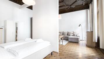 A modern hotel room with a large bed, a sofa, a desk, and a mirror.