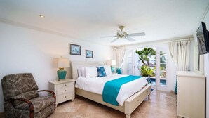 A bedroom with a bed, nightstands, a chair, a ceiling fan, and a view of the outdoors. - Villa with Pool & Golf Views - Coral Blu (2 bed) (Westmoreland)