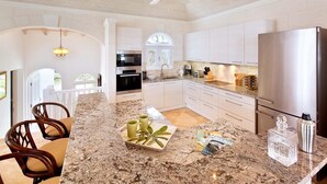 A modern kitchen with white cabinets, a stainless steel refrigerator, and a granite countertop. - Villa with Pool & Golf Views - Coral Blu (2 bed) (Westmoreland)