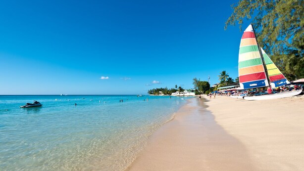 A beach with clear turquoise water, a sandy shore, and a colorful sailboat. - Villa with Pool & Golf Views - Coral Blu (2 bed) (Westmoreland)