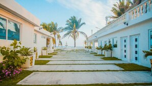 A pathway leading to a building with white walls and balconies, lined with palm trees and potted plants. - Hotel La Casona Beach (Iztapa)