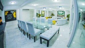 A modern, well-lit interior with a glass dining table surrounded by chairs, a white sofa, and a bench. - Hotel La Casona Beach (Iztapa)