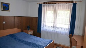 A bedroom with a wooden bed, a nightstand, a chair, and a window with curtains. - Lenardic Bled apartments for 5 person.  (Bled)