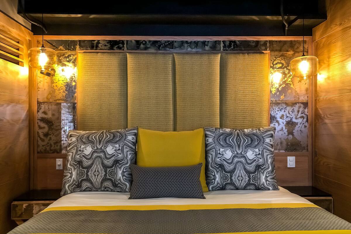 Un lit avec une couvre-lit à rayures jaunes et grises, deux coussins à motifs et un seul coussin gris.