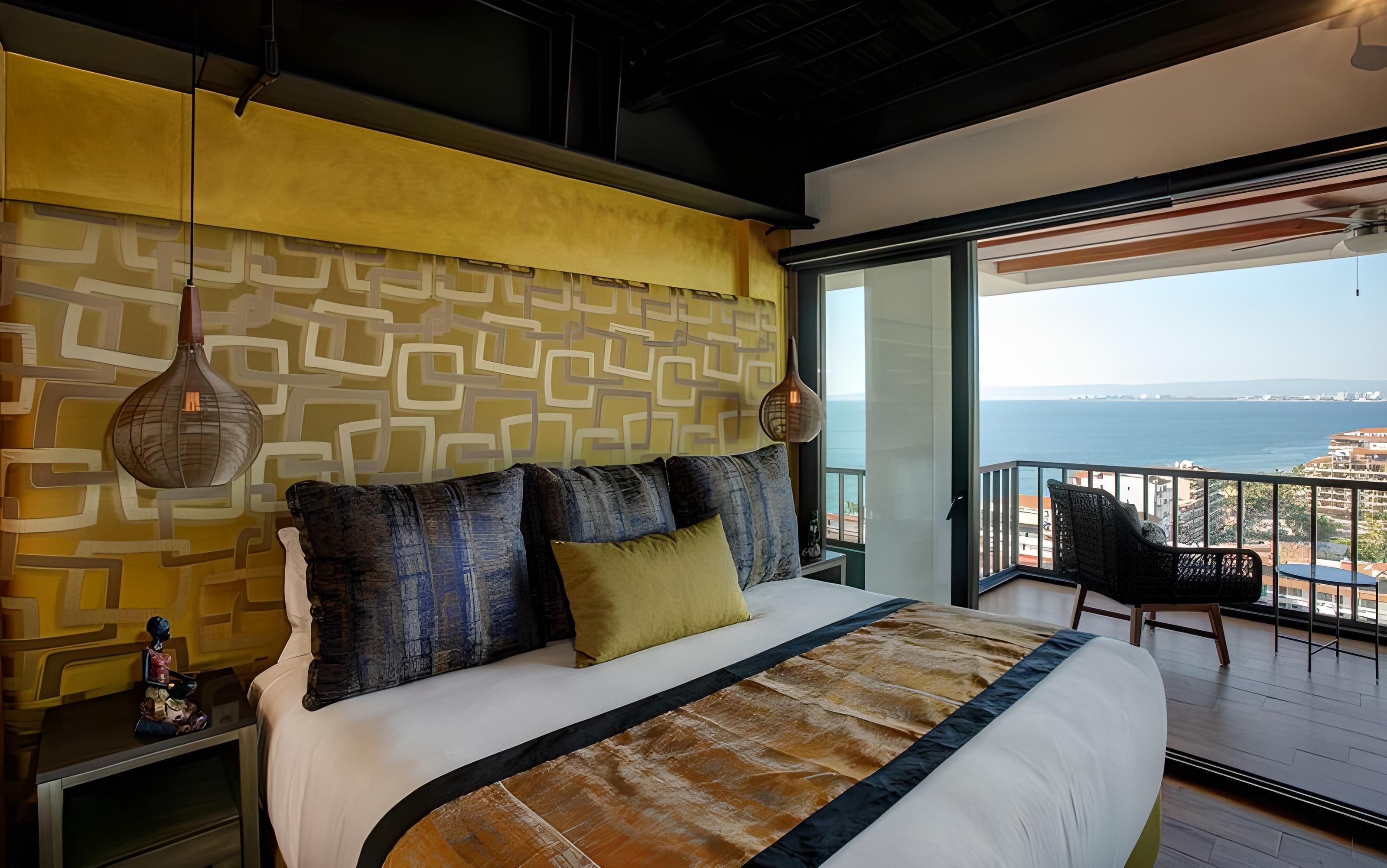 A modern bedroom with a large bed, patterned wallpaper, and a balcony with a view of the sea.