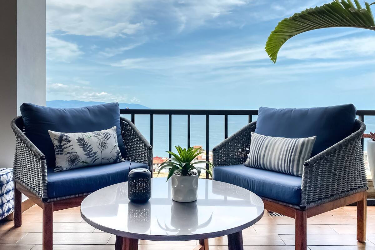 Un balcon avec deux fauteuils en osier, une petite table et une plante en pot.