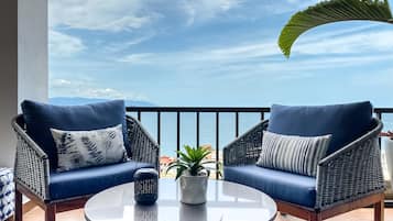 A balcony with two wicker chairs, a small table, and a potted plant.