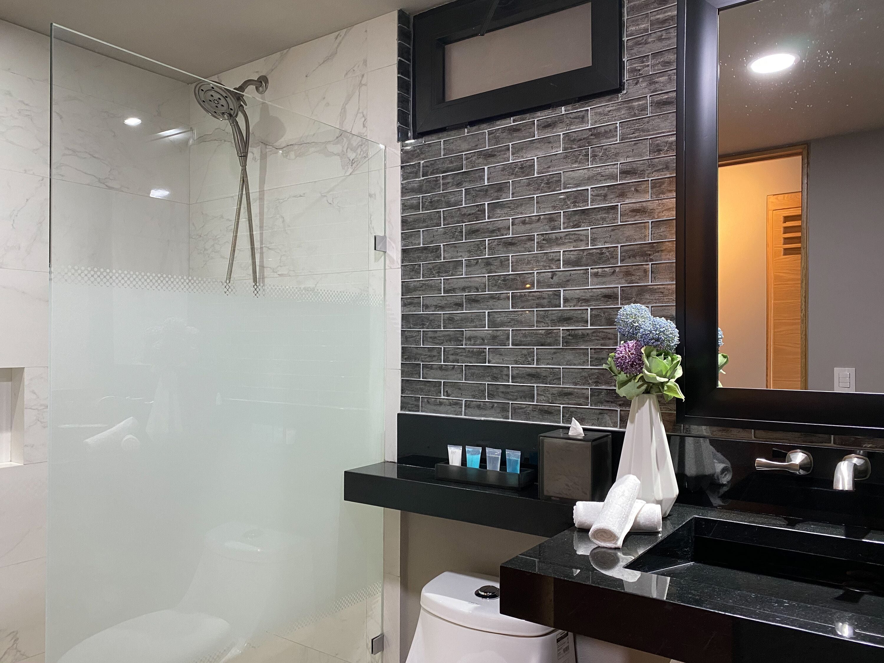 Un baño moderno con cabina de ducha de vidrio, tocador de mármol negro y espejo sobre el lavabo.