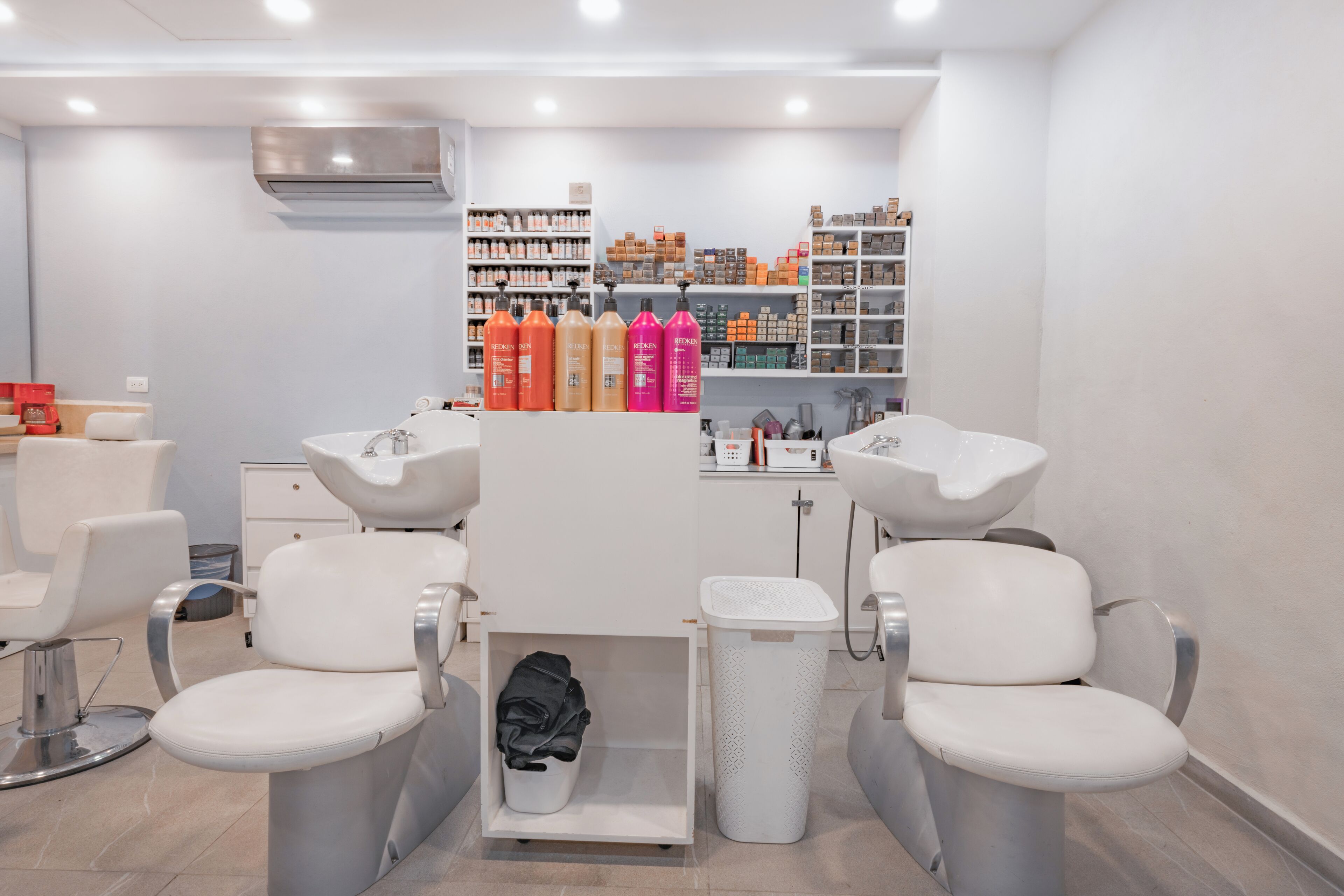 A modern salon with two white chairs, a sink, and shelves stocked with hair products.