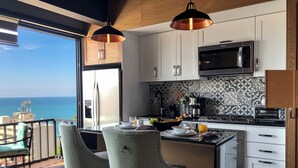 Une cuisine moderne avec vue sur la mer, comprenant un grand îlot central, des tabourets de bar et une machine à café.