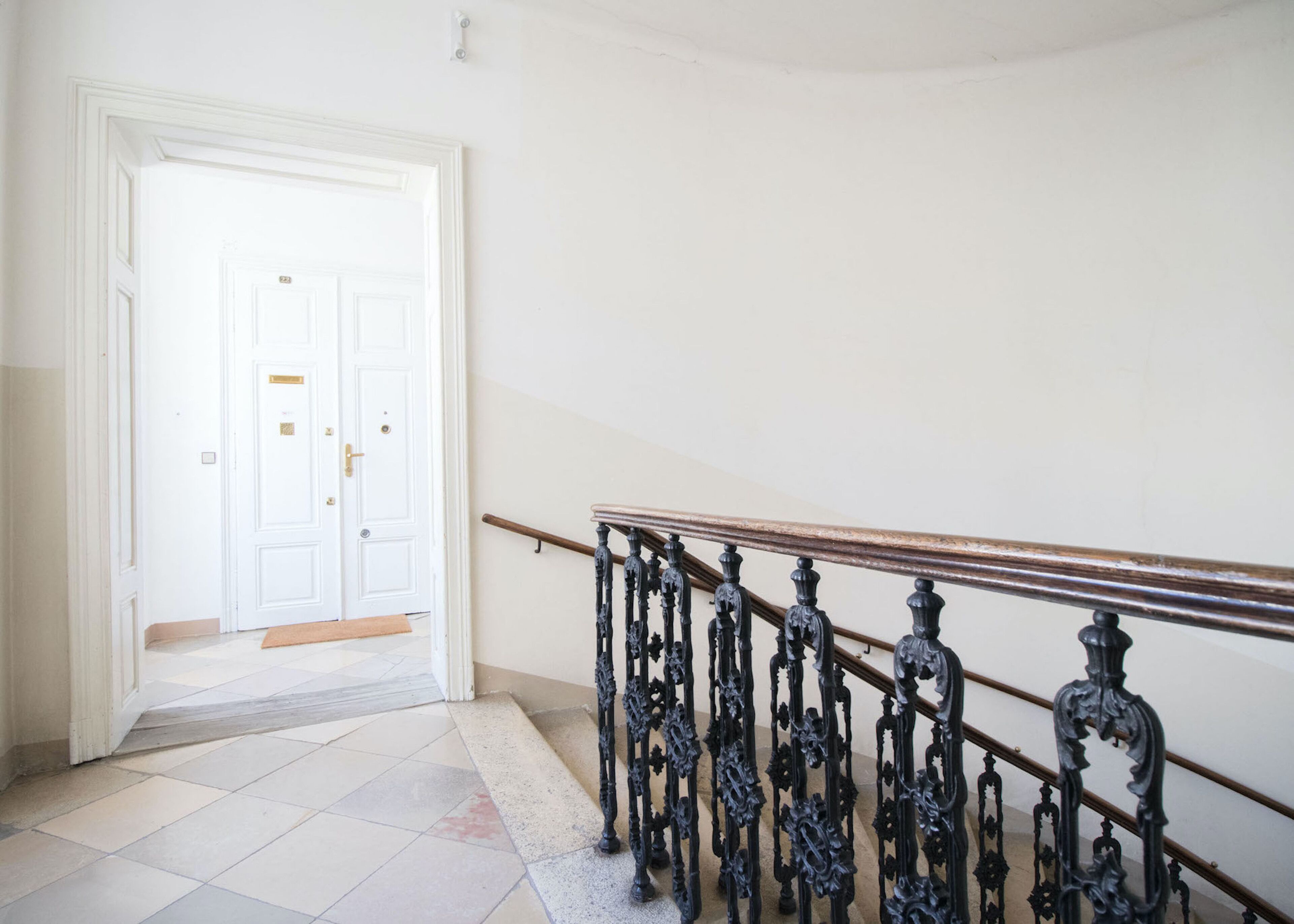A staircase with ornate black balusters and a wooden handrail, leading to a white door with a brass handle.