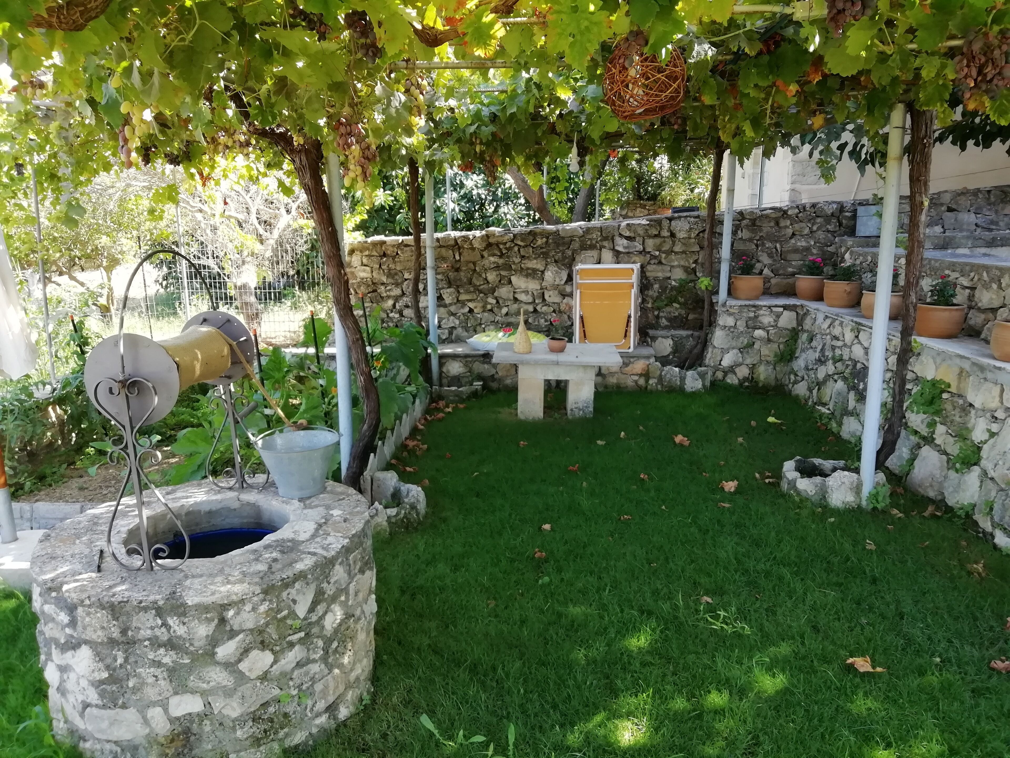 A stone well, a stone bench, and a stone wall with potted plants in a garden area.