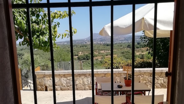 Un patio con una mesa y sillas, una sombrilla blanca y vistas a un paisaje montañoso a través de una reja de metal.