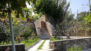 Una escalera de piedra que lleva a una puerta de madera, rodeada de exuberante follaje y un muro de piedra.