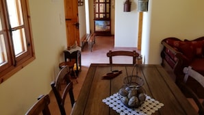 Un comedor acogedor con una mesa de madera, sillas y un centro de mesa decorativo. Se ve un banco de madera y un sofá rojo al fondo.