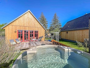 A wooden cabin with a hot tub, outdoor seating, and a fenced yard.