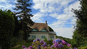 A house with a white exterior and green trim, surrounded by lush greenery and purple hydrangeas. - Rental of a Cottage + an Apartment in a Norman character property (Veulettes-sur-Mer)