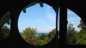 A view through a window with a circular frame, revealing a landscape with trees and a distant body of water. - Rental of a Cottage + an Apartment in a Norman character property (Veulettes-sur-Mer)