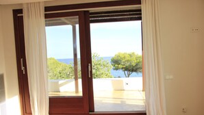 A room with a large sliding glass door leading to a balcony with a view of the sea and trees. - Spectacular tower in front of the sea (L' AMETLLA DE MAR)