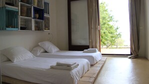 A hotel room with two beds, a wooden floor, a large window with curtains, and shelves with baskets. - Spectacular tower in front of the sea (L' AMETLLA DE MAR)