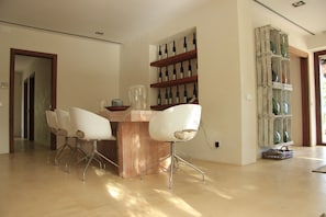 A dining area with a wooden table and four white chairs, a wine rack on the wall, and a basket on the floor.