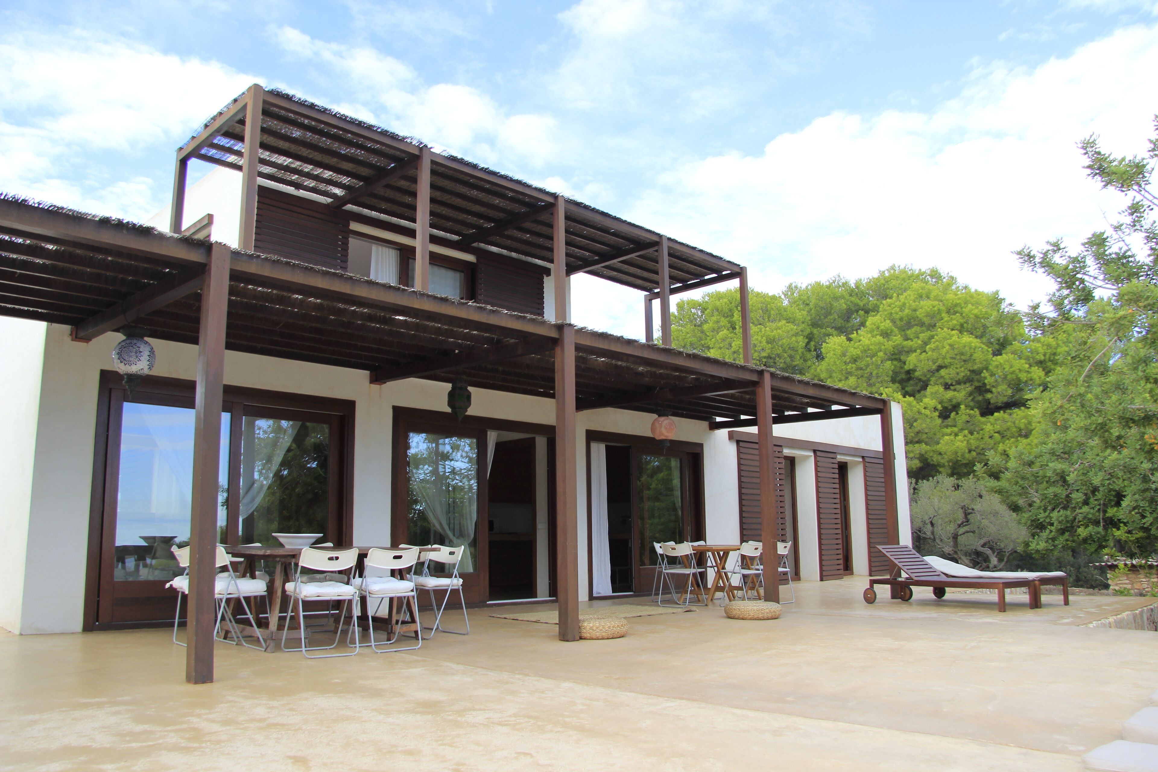 A modern two-story building with a covered patio area featuring outdoor seating and a lounge chair.