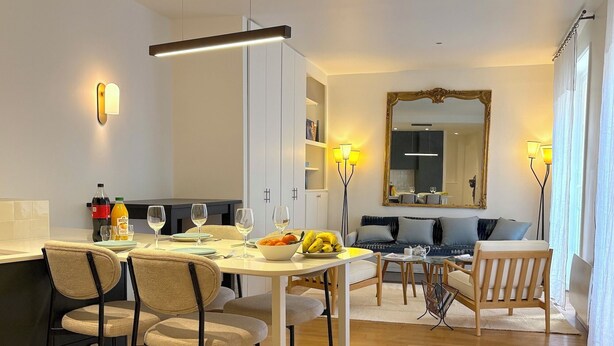 Un salon moderne comprenant un coin repas, un plancher en bois et un grand miroir mural.