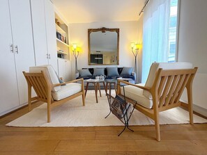 A modern living room with two wooden chairs, a sofa, a coffee table, and a large mirror. - L'appartement Magdebourg (Paris)