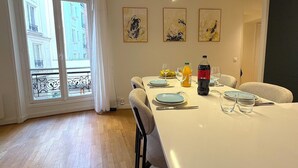 Un coin repas avec une table dressée pour quatre personnes, une bouteille de soda et une bouteille de jus d’orange. Trois œuvres d’art encadrées ornent le mur.