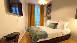 Une chambre d’hôtel avec un lit, un bureau, une télévision, une bibliothèque et un balcon avec des rideaux.