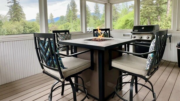 En täckt uteplats med ett bord och stolar, en grill och utsikt över träd och berg.