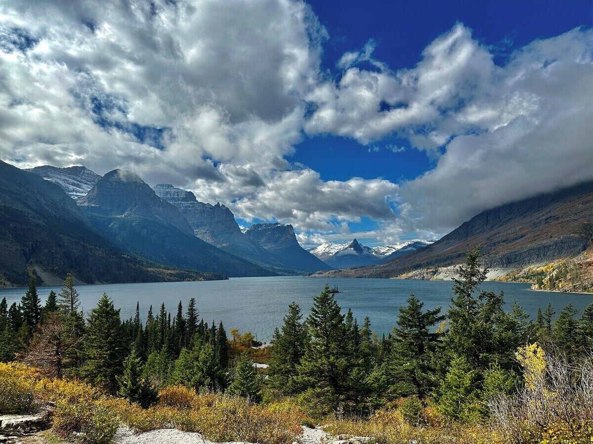 Un paysage montagneux avec un lac, entouré de forêts denses et de sommets enneigés.