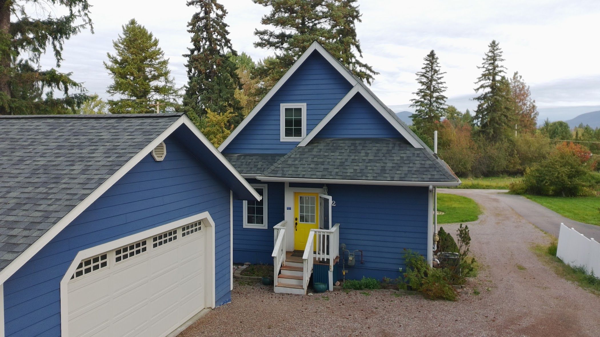 Ein zweistöckiges Haus mit blauer Fassade, einer Veranda und einer Auffahrt zu einer Garage.