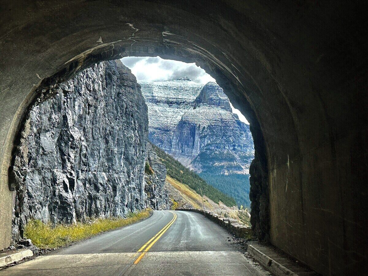 Un tunnel traversé par une route, entouré de falaises rocheuses et de montagnes.