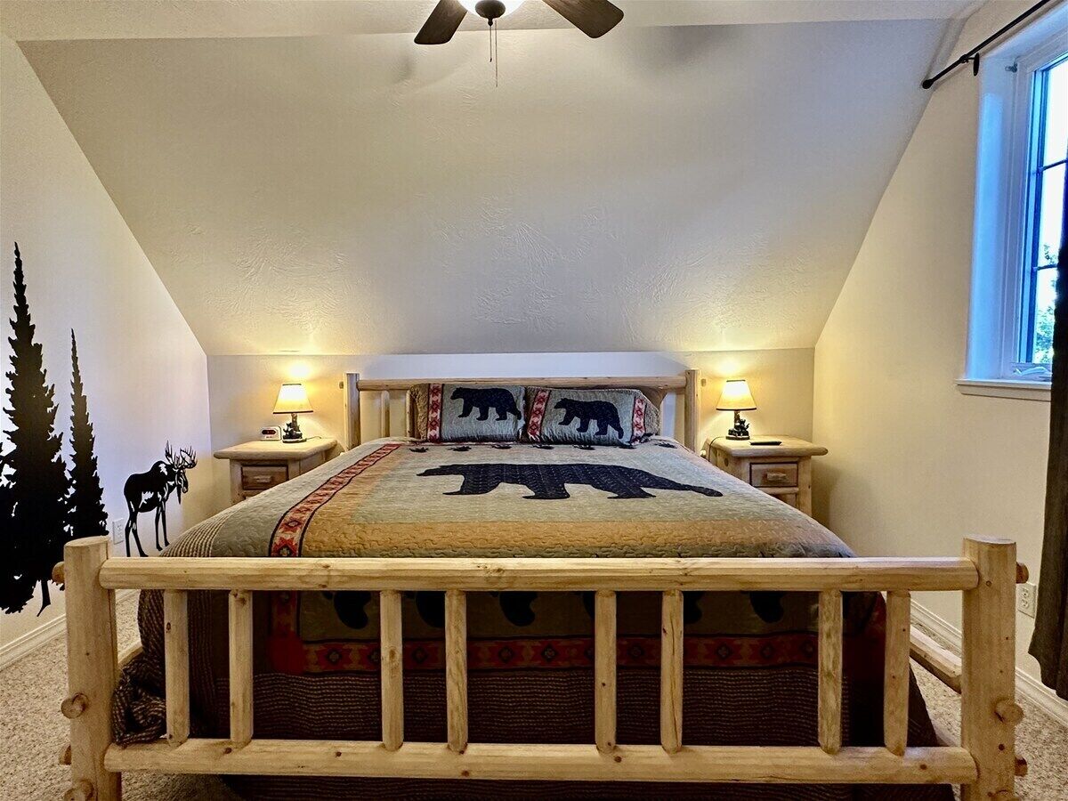 A bedroom with a wooden bed frame, a ceiling fan, two bedside lamps, and a window with daylight.