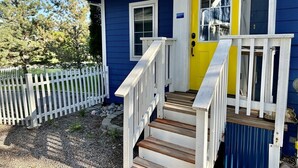 Ett tvåvåningshus med ett vitt staket, en gul ytterdörr och en trätrappa som leder upp till verandan.