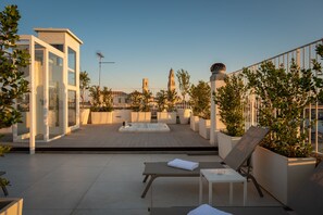 En takterrass med ett bubbelbad, solstolar och krukväxter.