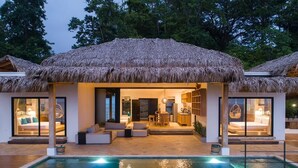 Una villa moderna con piscina, construcciones de techo de paja e interiores bien iluminados.