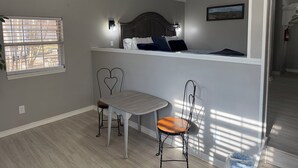 A bedroom with a bed, bedside table, two chairs, a ceiling fan, and a window with blinds.