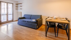 En moderne stue med en grå sofa, et træspisebord dækket til fire personer, og en pendel lampe over.