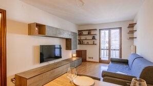 En moderne stue med et fladskærms-tv, møbler i træ, et spisebord dækket med tallerkener og glas, samt en sofa.