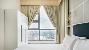 Hotellihuone, jossa on suuri sänky, vaatekaappi ja ikkunasta avautuva näkymä kaupunkiin sekä kaupunkimaisema, joka on nähtävissä ulkona.