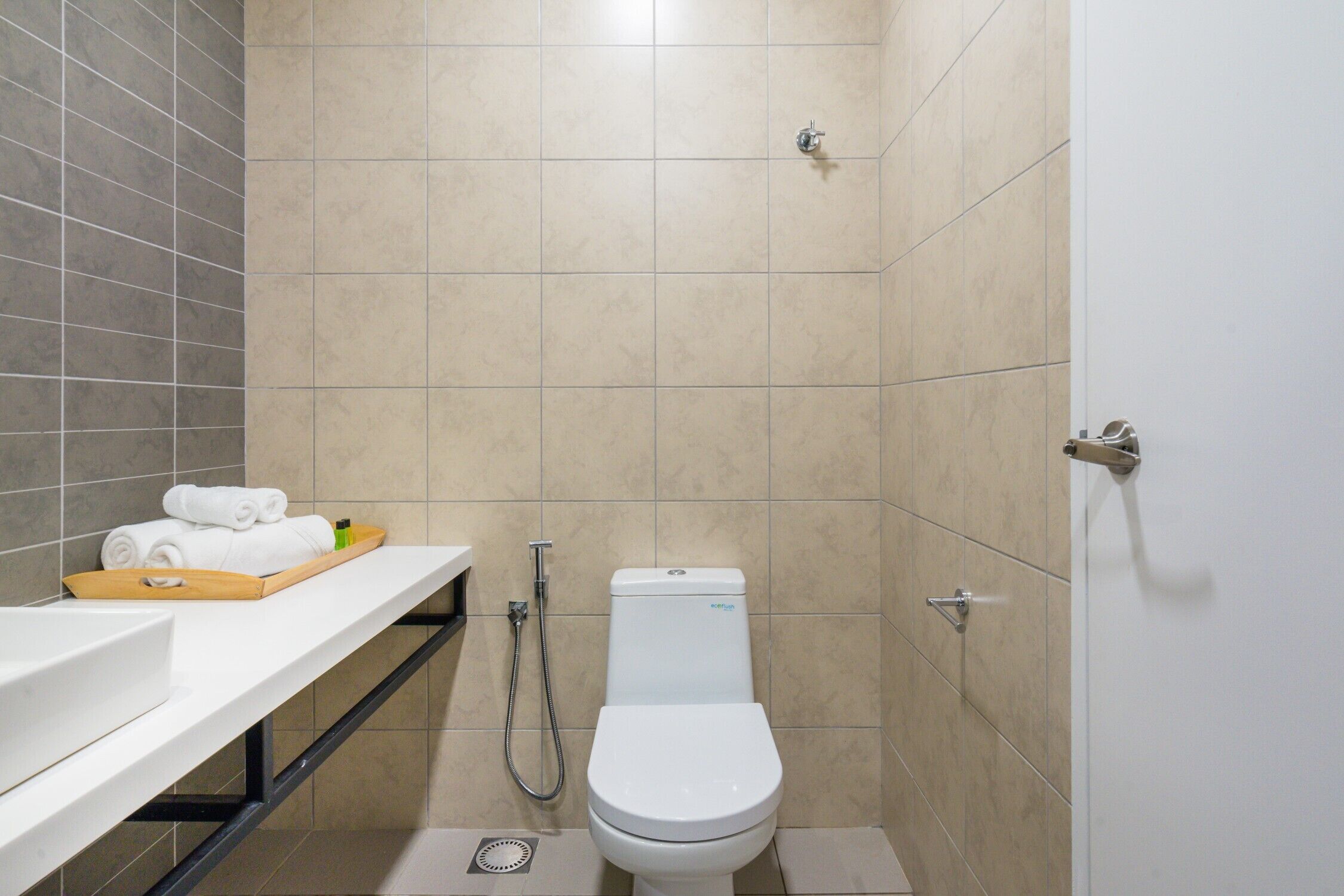 A modern bathroom with a white toilet, a shower, and a vanity with a tray of towels.