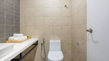 A modern bathroom with a white toilet, a shower, and a vanity with a tray of towels.