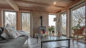 Een gezellige woonkamer met een bank, een glazen salontafel, een open haard en grote ramen met uitzicht op bomen.