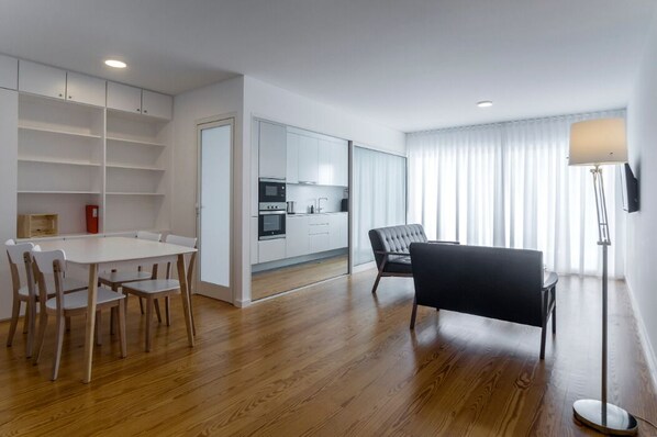 A modern apartment with a dining area, kitchen, and a large window with curtains.