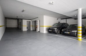 A parking garage with two cars parked, white walls, and yellow safety lines.