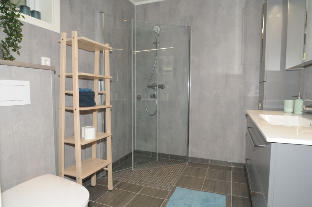 Un baño moderno con cabina de ducha de vidrio, estante de madera y lavamanos con espejo.