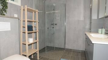 Un baño moderno con cabina de ducha de vidrio, estante de madera y lavamanos con espejo.