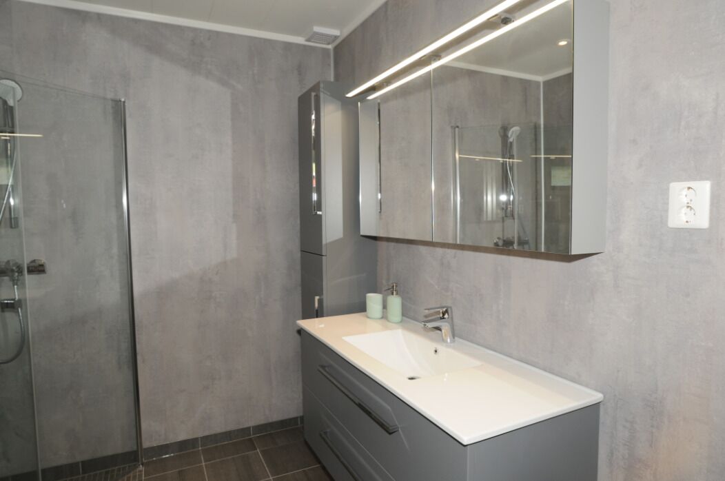 A modern bathroom with a large mirror, a white sink, and a shower enclosure.